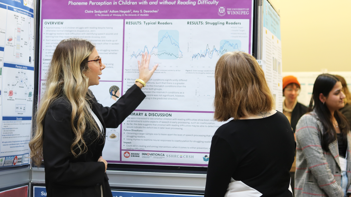 Two students stand in front of a poster discussing research.