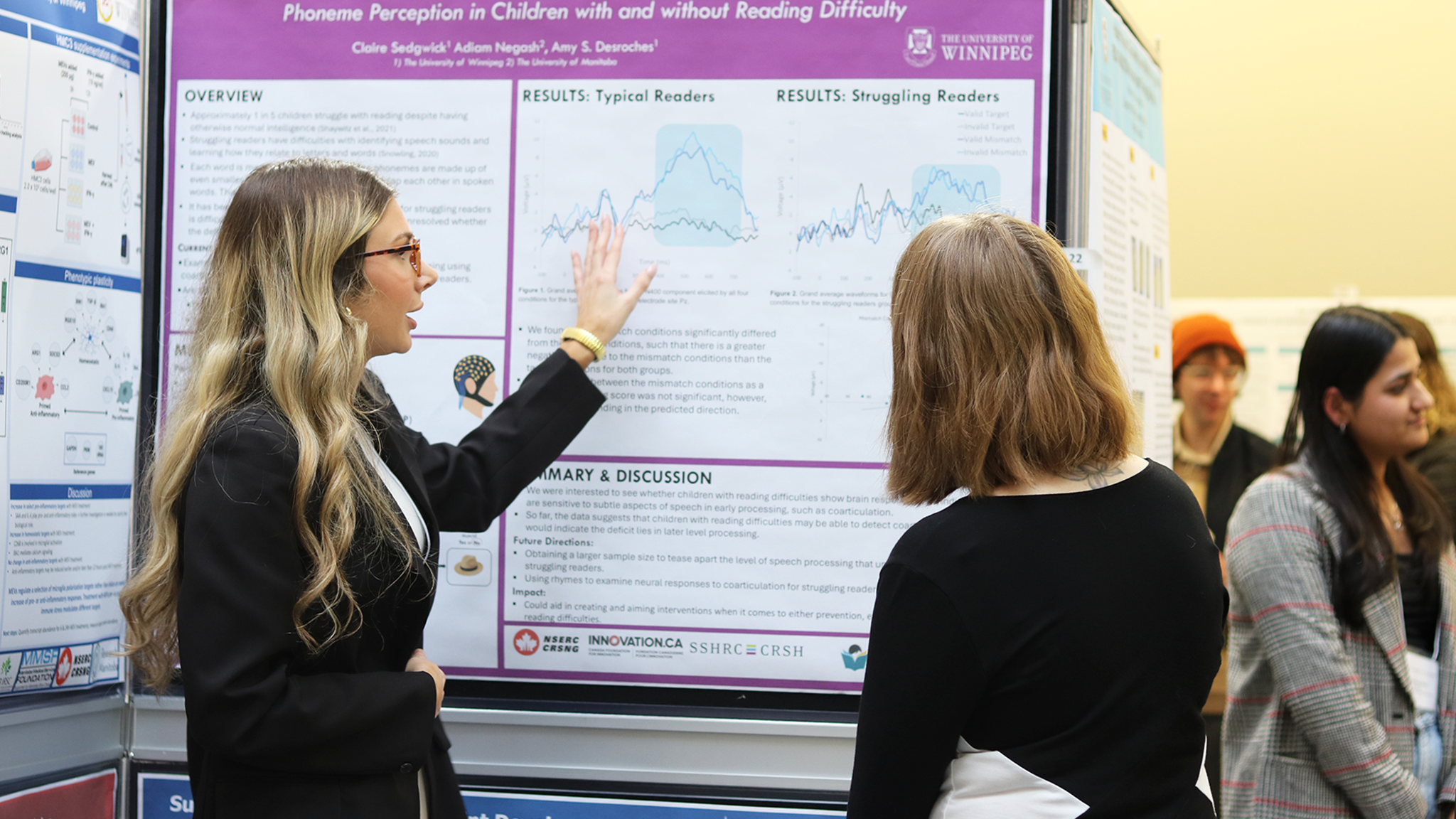 Two students stand in front of a poster discussing research.