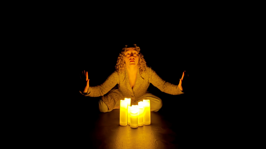 Actor Elli Suppes sits on a dark stage with lit candles.