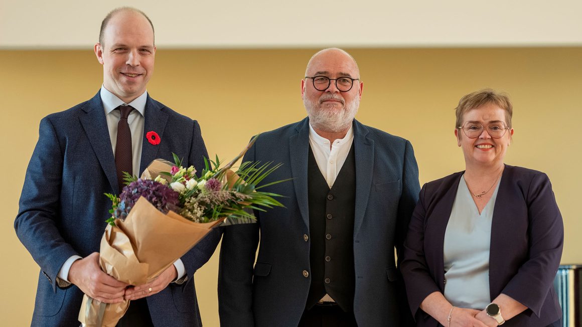 Dr. Ryan Eyford holding a bouquet of flowers standing next to Logi Einarsson, Iceland’s Minister of Culture, Innovation, and Higher Education and Silja Bára R. Ómarsdóttir, Rector (i.e., President) of the University of Iceland.