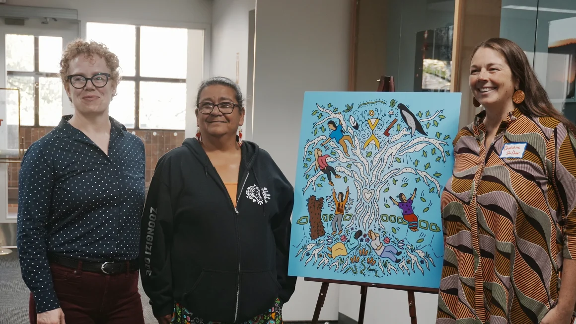 People standing next to an easle with artwork on it.