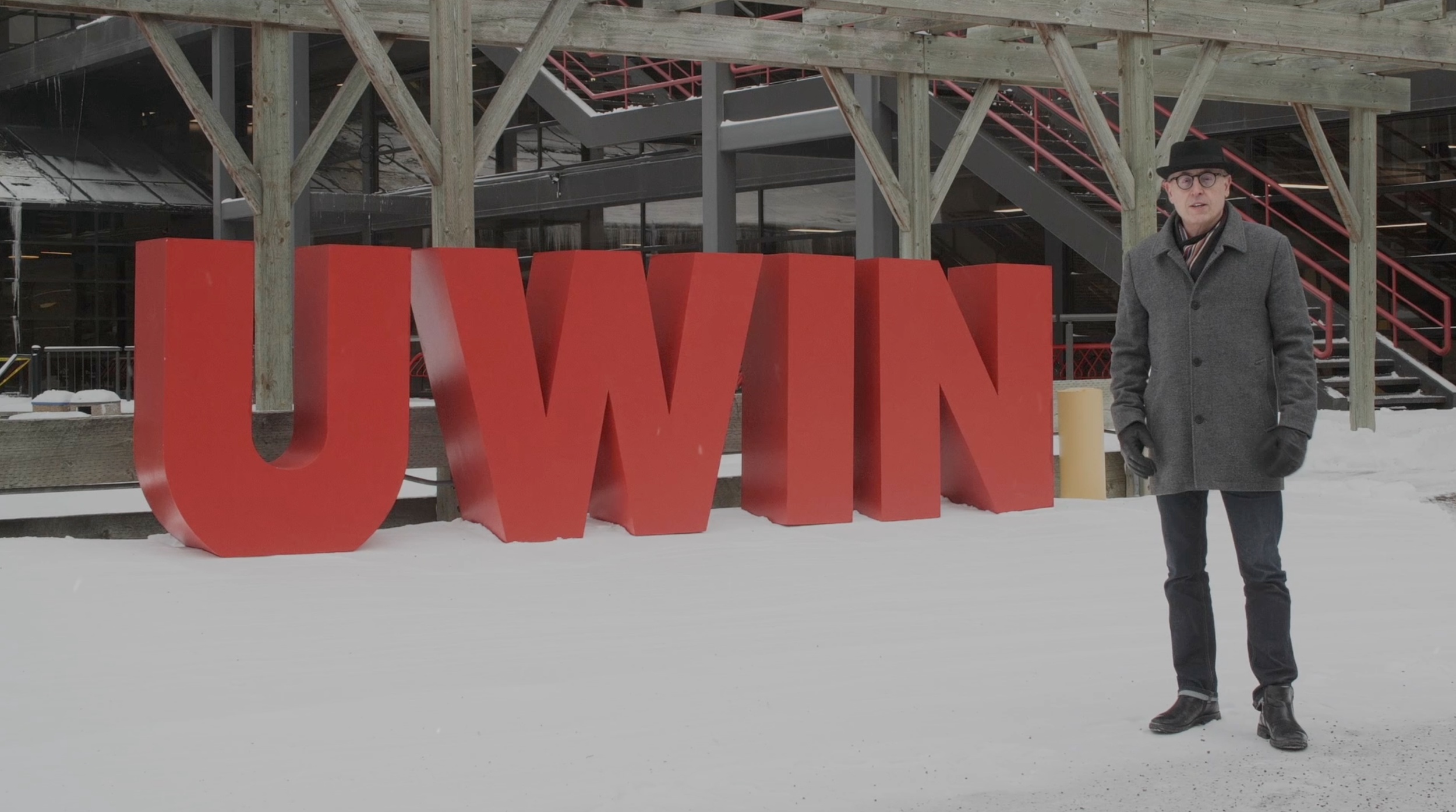 UWinnipeg interim president Jino Distasio standing in the snow in front of red UWIN sign