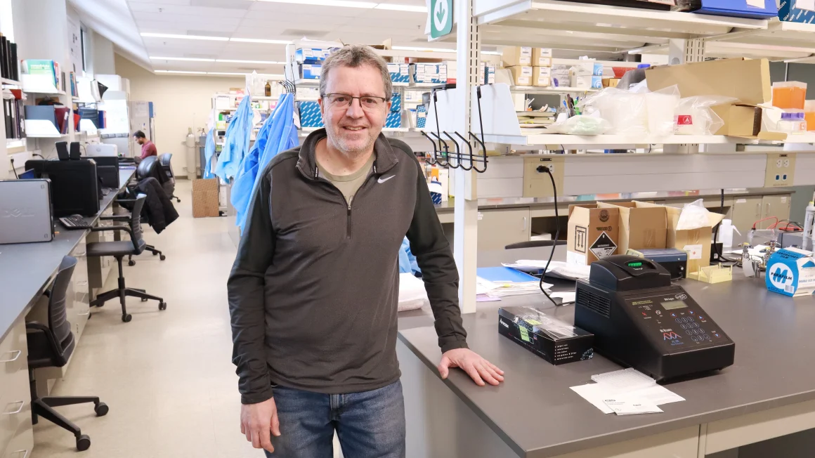 A man in a grey shirt and jeans stands in a biology laboratory.