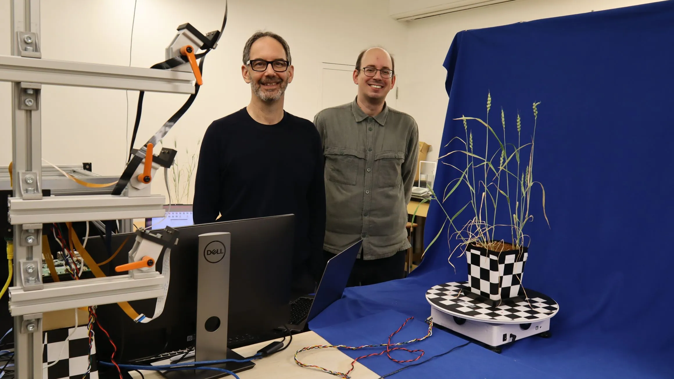 Two men stand in a lab in front of a plant turntable and camera setup.