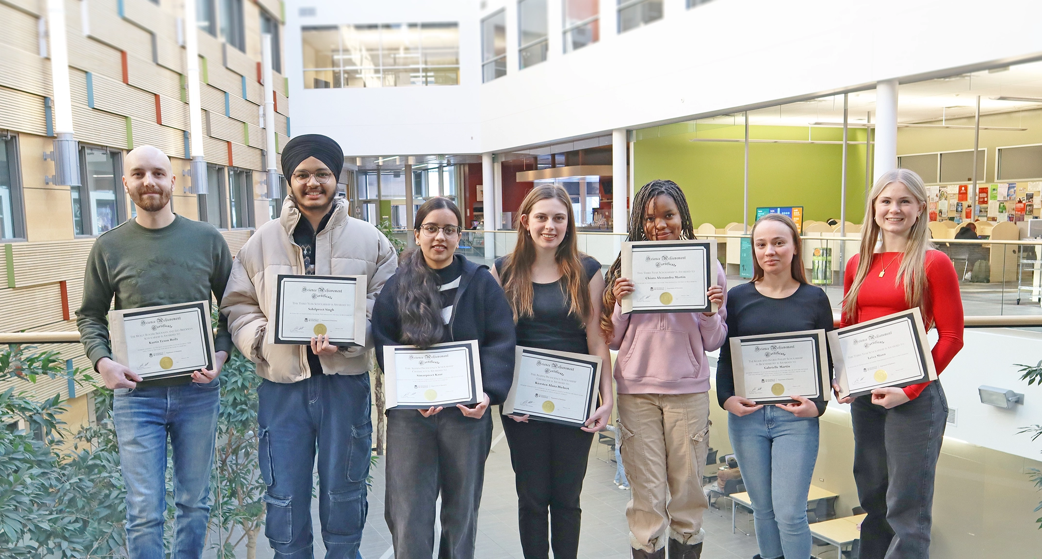 Chemistry award recipients Kurtis Boily, Sahilpreet Singh, Simarpreet Kaur, Kiersten Hiebert, Chiara Martin, Gabrielle Martin, Leiva Mann stand with their awards in an atrium.
