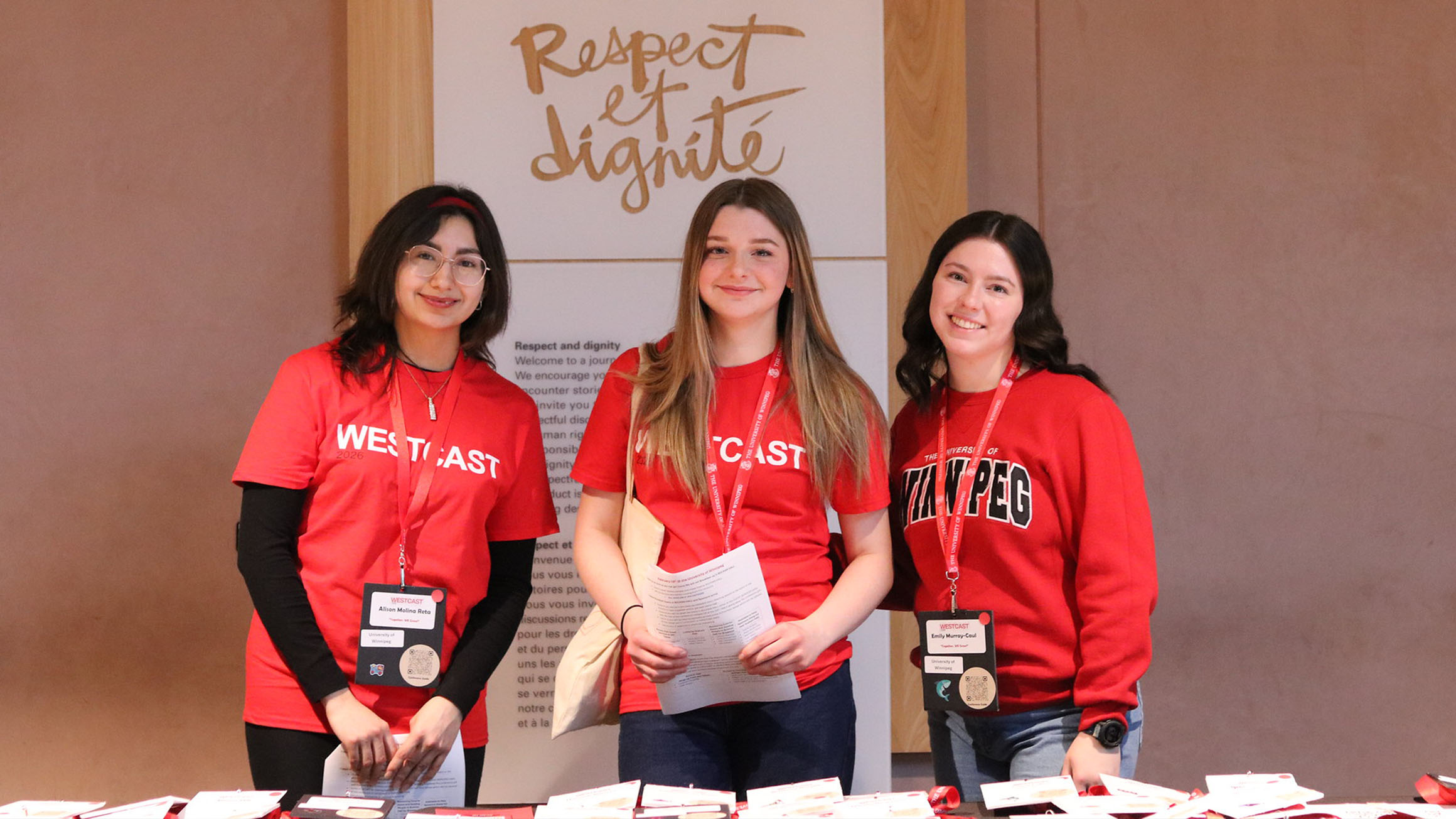 Alison Molina Reta, Lola Hebert, and Emily Murray-Caul standing in front of a sign in french that says respect and dignity