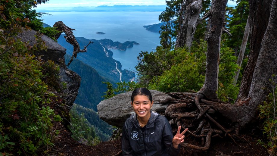 Allyz Tabirara outside on a hill, in a forest with the Pacific Ocean in the background