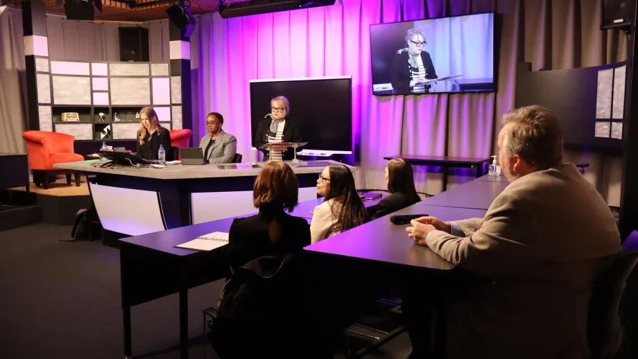 Panelists speak on stage in front of a purple background with audience members in the foreground.