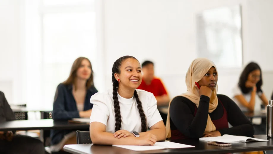 Several students sit at desks in a classroom with a white background.
