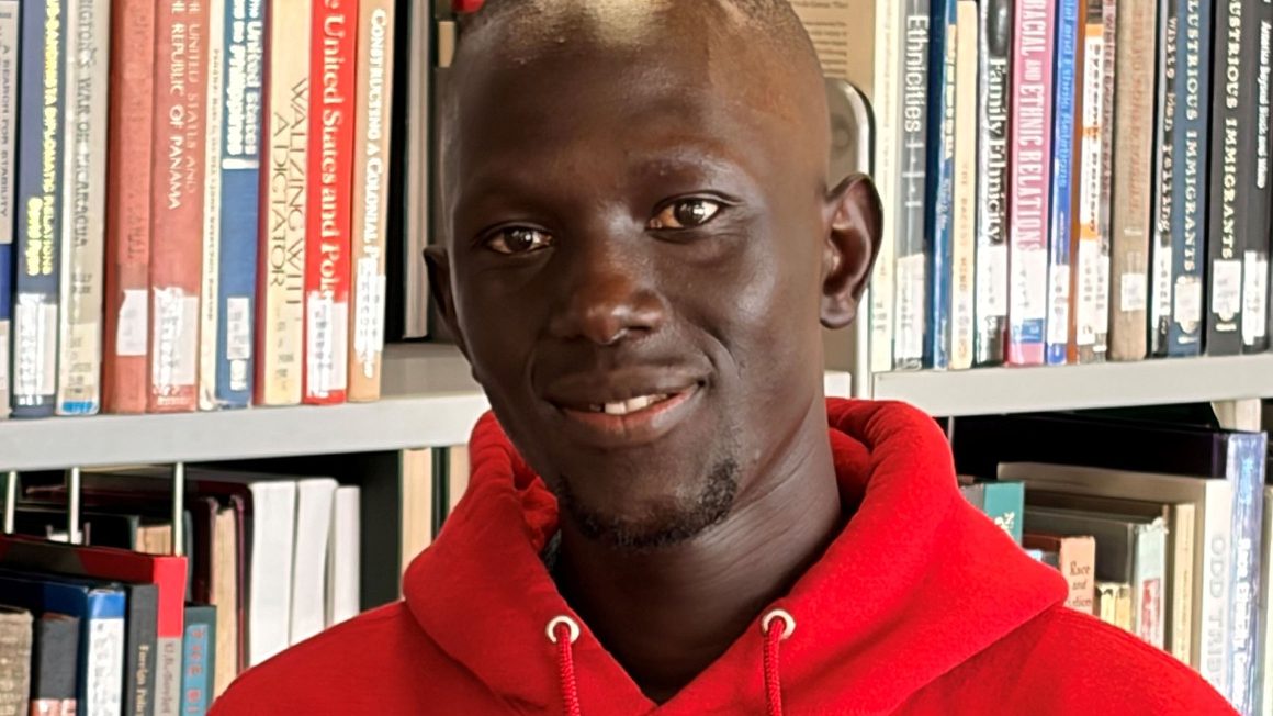 Sunday Emmanuel, wearing a red Wesmen jersey in front of a stack of library books.
