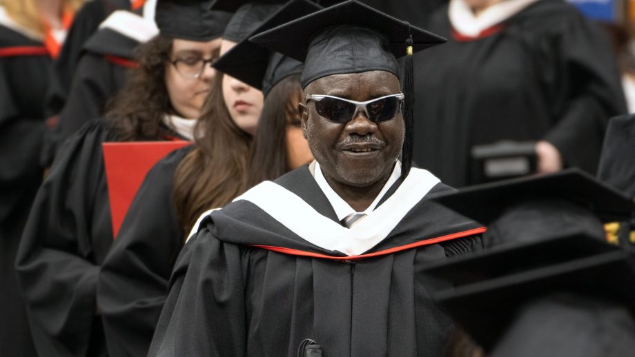 Ibrahim Youssif in his graduation procession wearing his cap and gown and a smile.