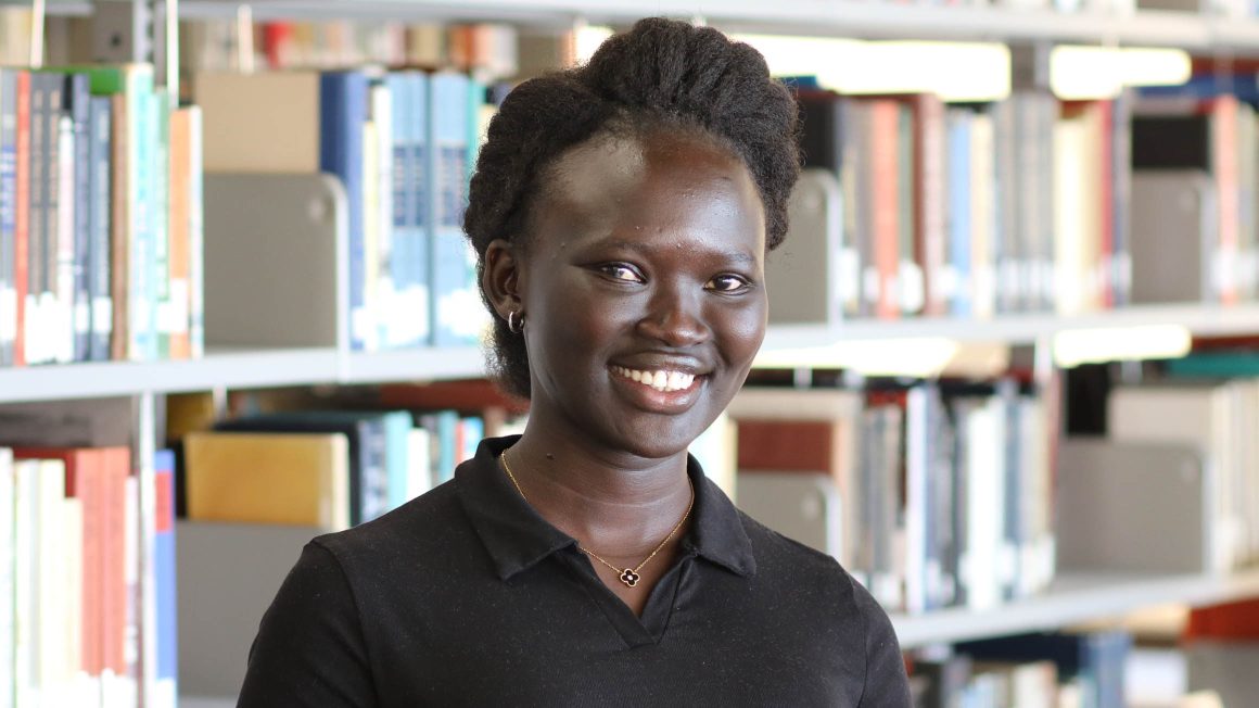 Monica Ayuen Dot standing in front of library stacks