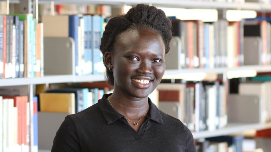Monica Ayuen Dot standing in front of library stacks