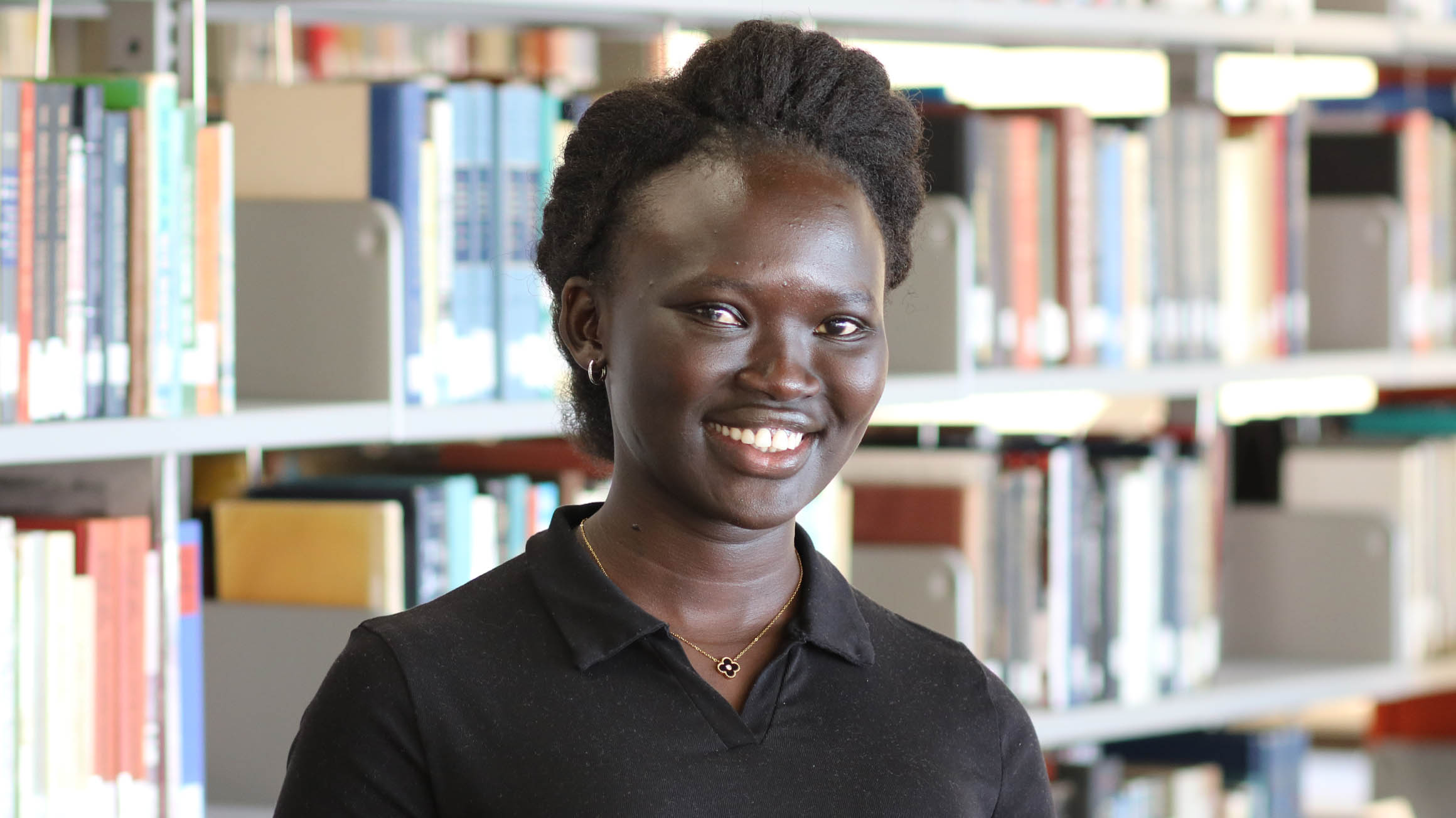 Monica Ayuen Dot standing in front of library stacks
