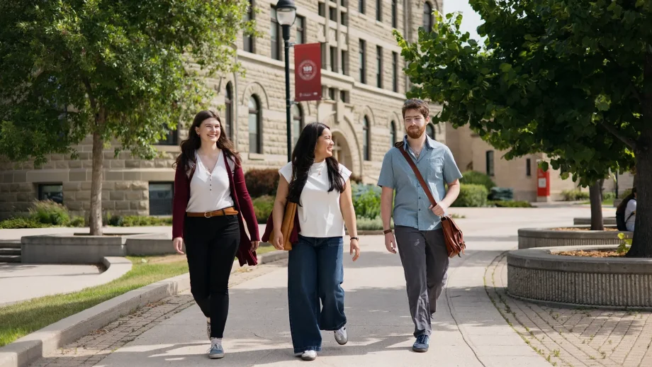 Three students walk on the sidewalk on campus.