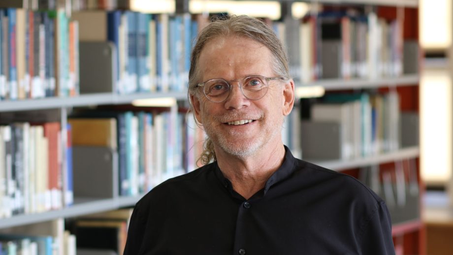 Dr. Lloyd Kornelson standing in front of stacks of books in the library.