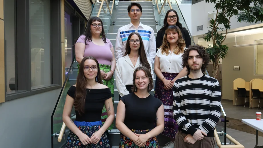 Eight students pose for a group photo on a staircase in an atrium.